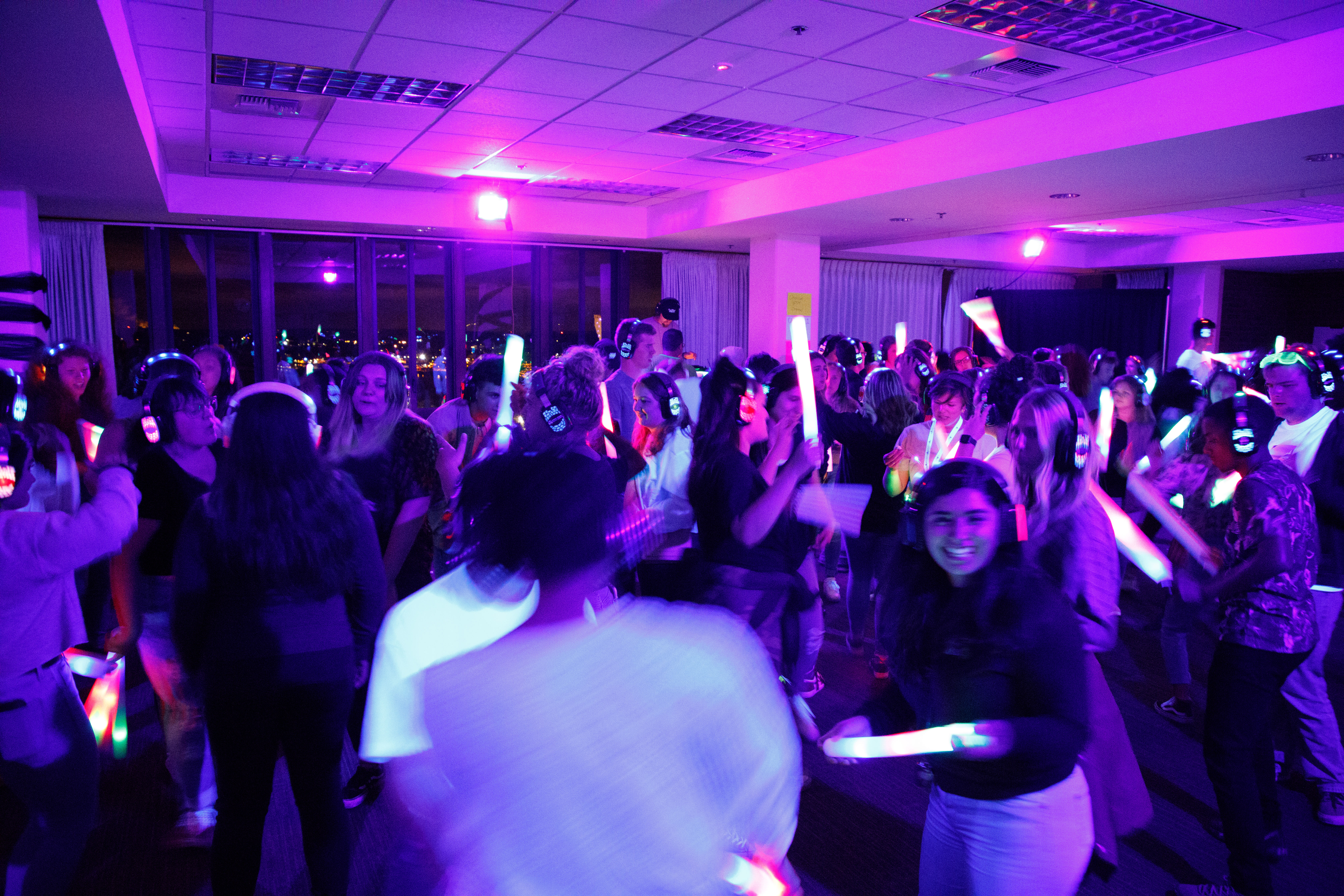 Image of the dance floor of the silent disco, many students are dancing and wearing wireless headphones lit up with colors and patterns.
