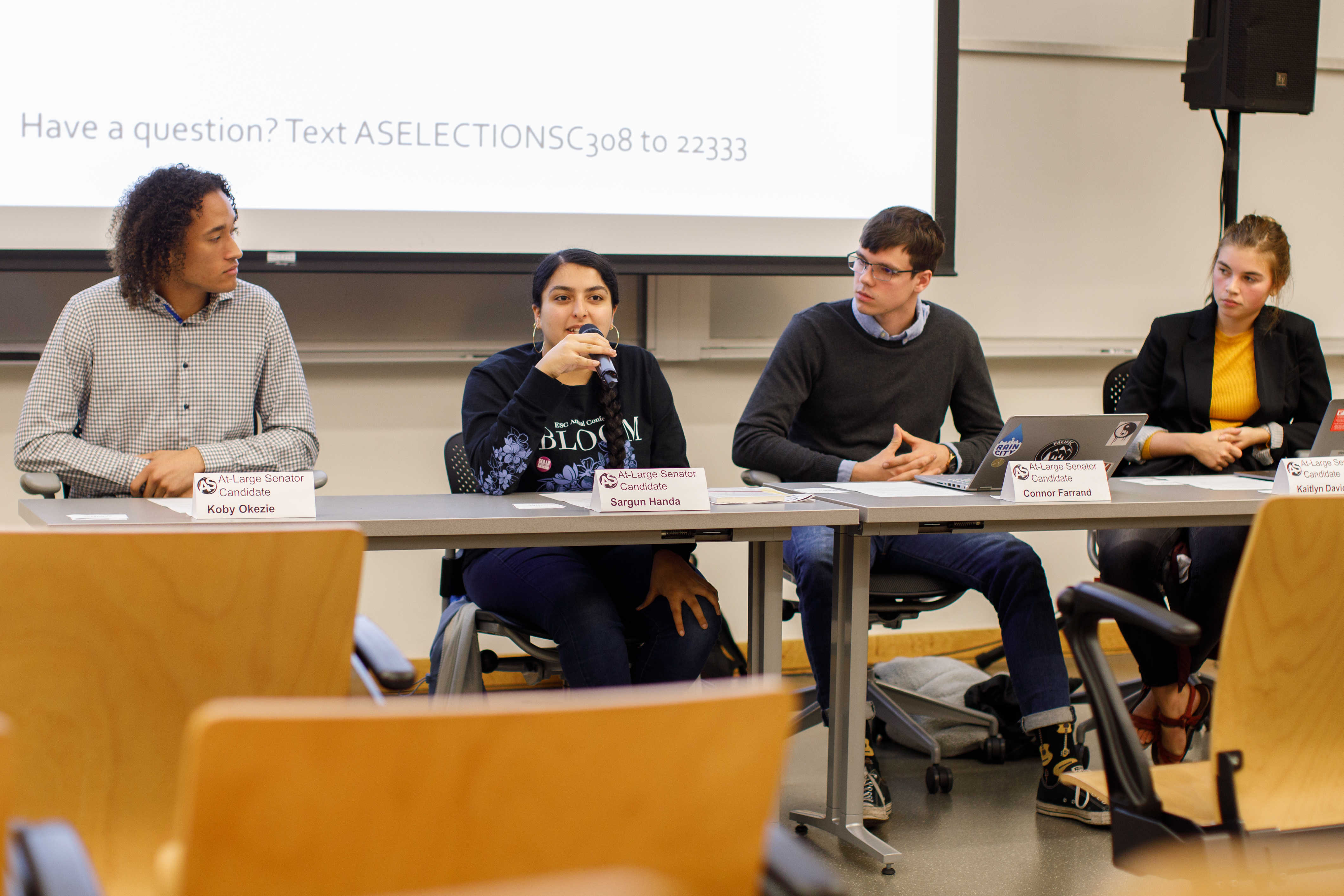 Image of the four candidates sitting on a panel, Sargun Handa is speaking into the microphone.