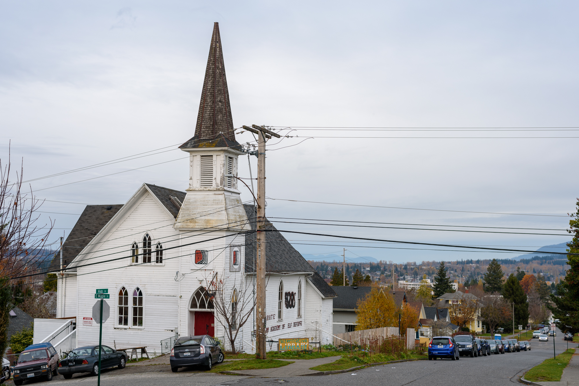 Image of the exterior of the Alternative Library, the building is an old church with a steeple. In front of the building is a sign that reads “Alternative Library”.