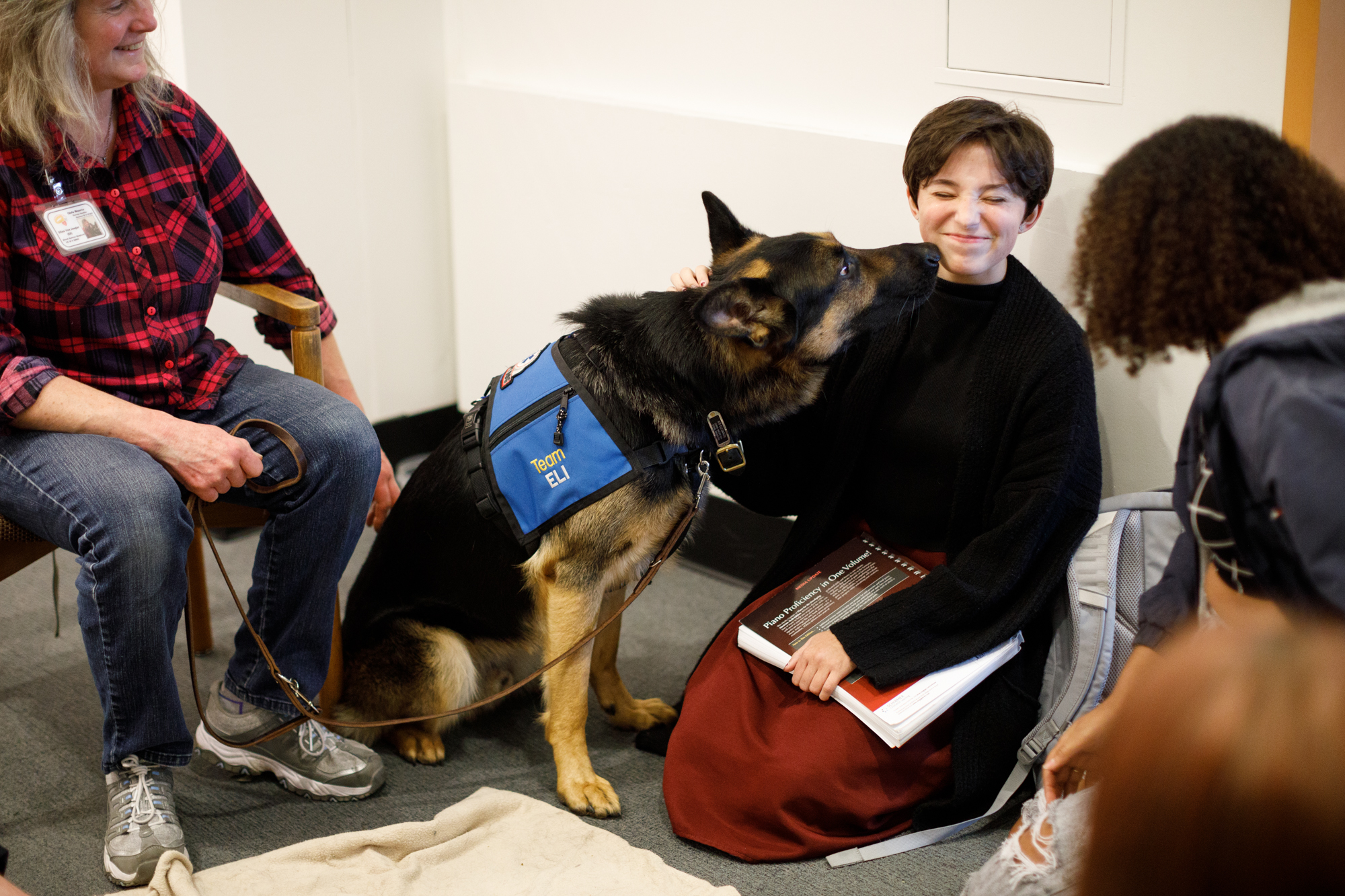 Image of Eli the German Shepherd reaching over to lick Kiana Doyle while they are both seated on the ground in the Wilson Library.